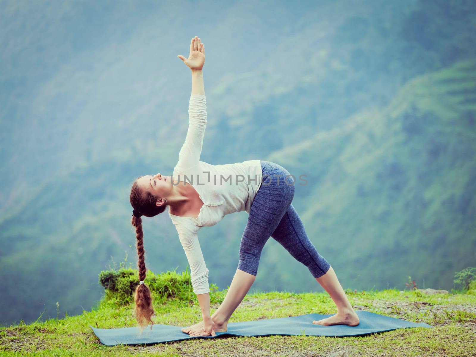 Vintage retro effect hipster style image of woman doing Ashtanga Vinyasa yoga asana Parivrtta trikonasana - revolved triangle pose outdoors