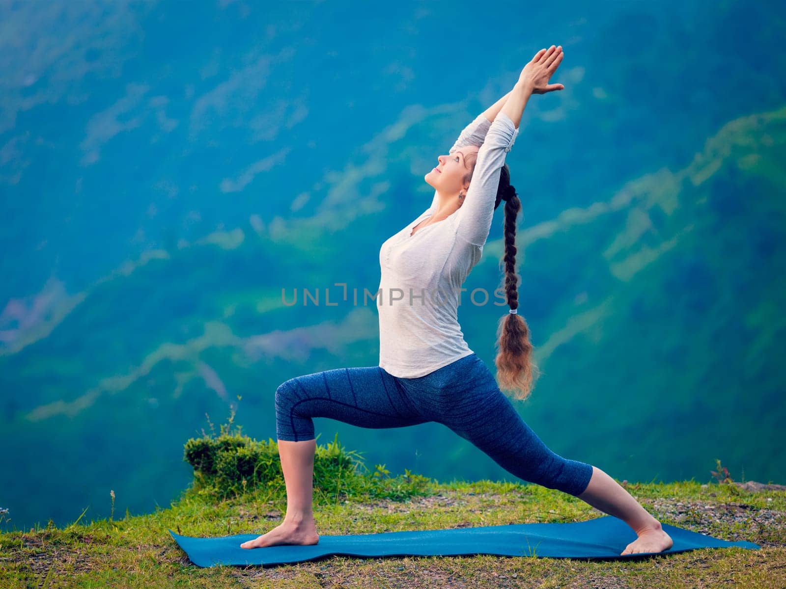 Woman doing yoga asana Virabhadrasana 1 - Warrior pose outdoors by dimol