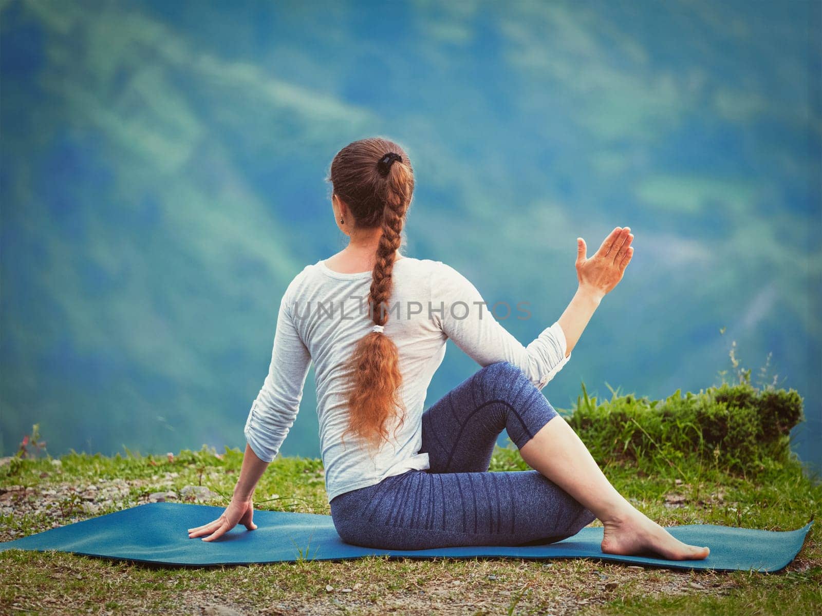 Hatha yoga outdoors - sporty fit woman doing yoga asana Parivrtta Marichyasana (or ardha matsyendrasana) - seated spinal twist outdoors in mountains. Vintage retro effect filtered hipster style image.