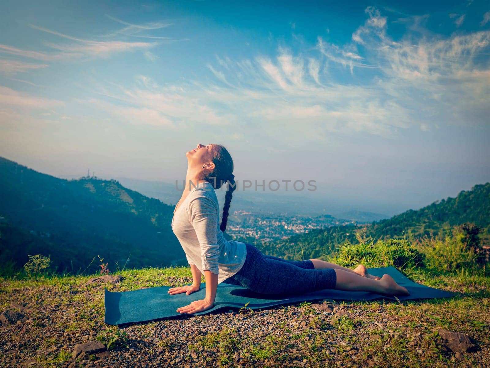 Yoga outdoors - woman practices Ashtanga Vinyasa yoga Surya Namaskar Sun Salutation asana Urdhva Mukha Svanasana upward facing dog pose in mountains in the morning. Vintage retro effect filtered image