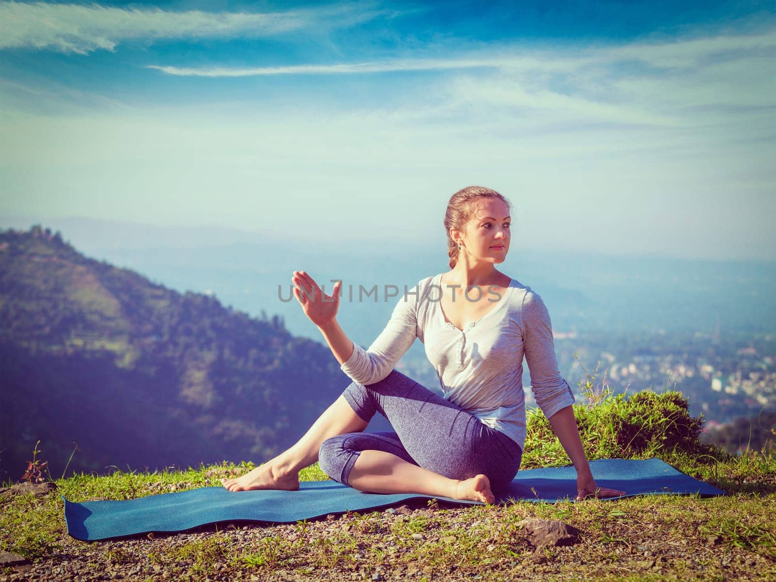 Yoga exercise outdoors - woman doing Ardha matsyendrasana asana - half spinal twist pose mountains in Himalayas in India in the morning. Vintage retro effect filtered hipster style image.