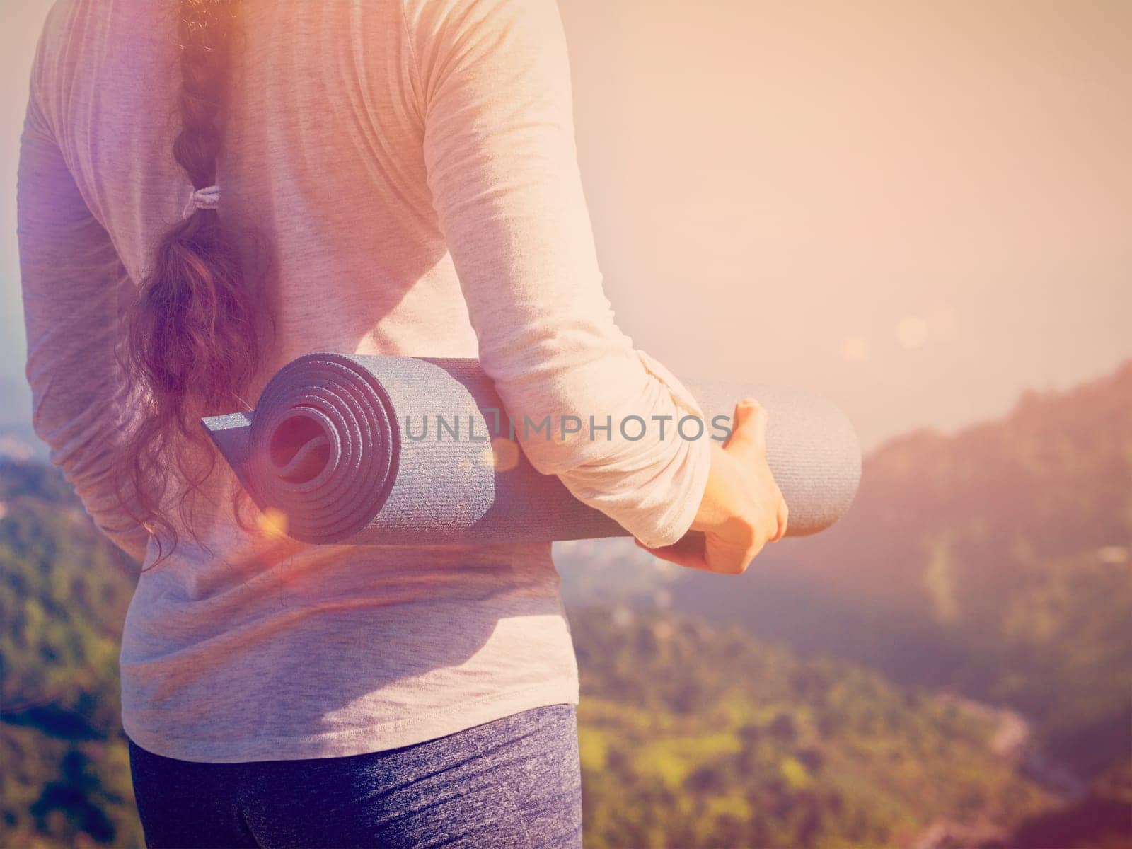 Woman standing with yoga mat outdoors in mountains close up with copyspace. With light leak and lens flare. Vintage retro effect filtered hipster style image.