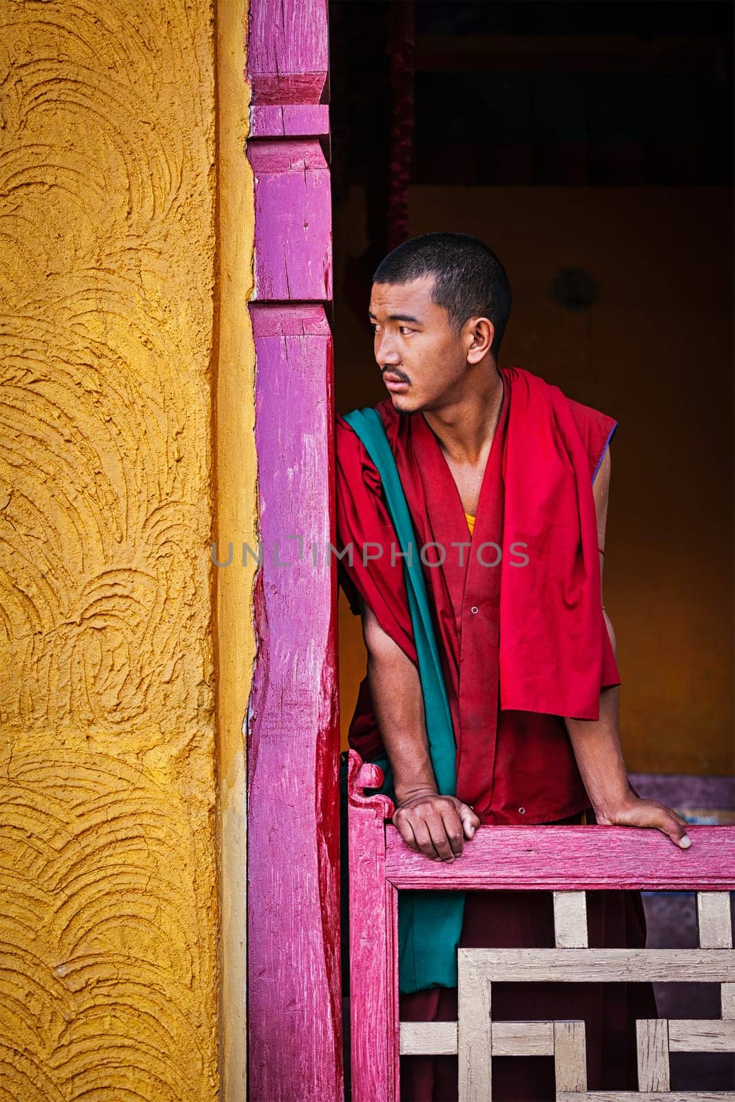 Young Buddhist monk standing in doorway of monastery by dimol