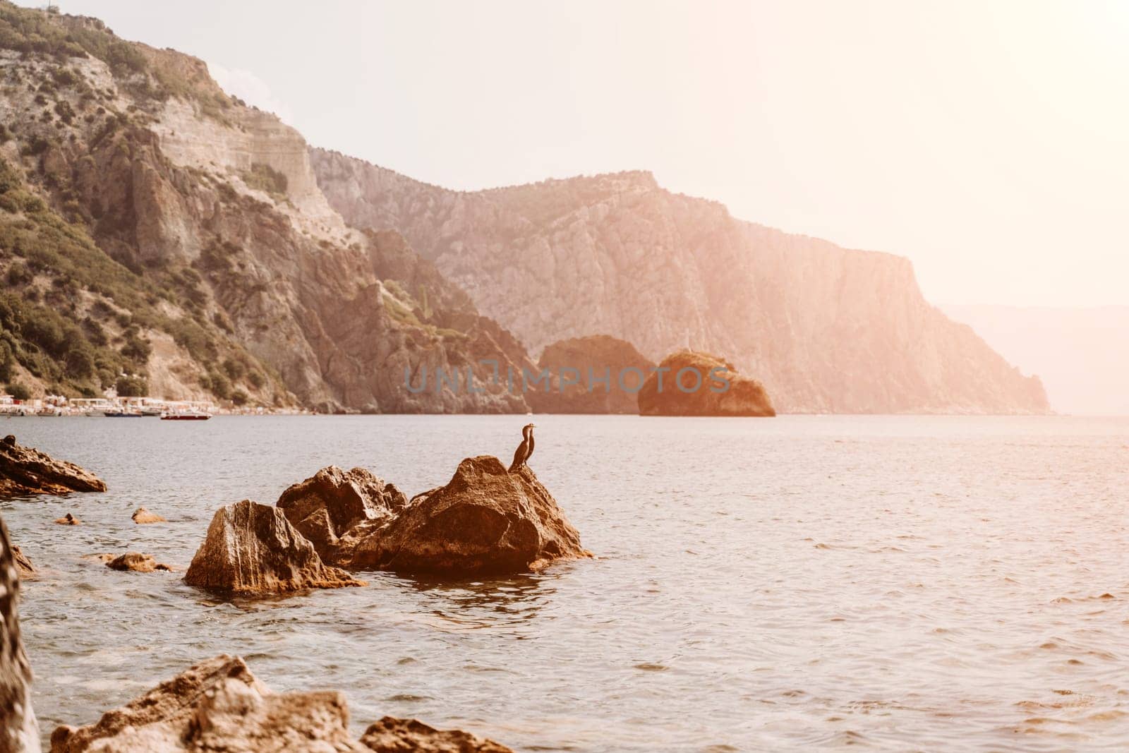 Yoga on the beach. A happy woman meditating in a yoga pose on the beach, surrounded by the ocean and rock mountains, promoting a healthy lifestyle outdoors in nature, and inspiring fitness concept