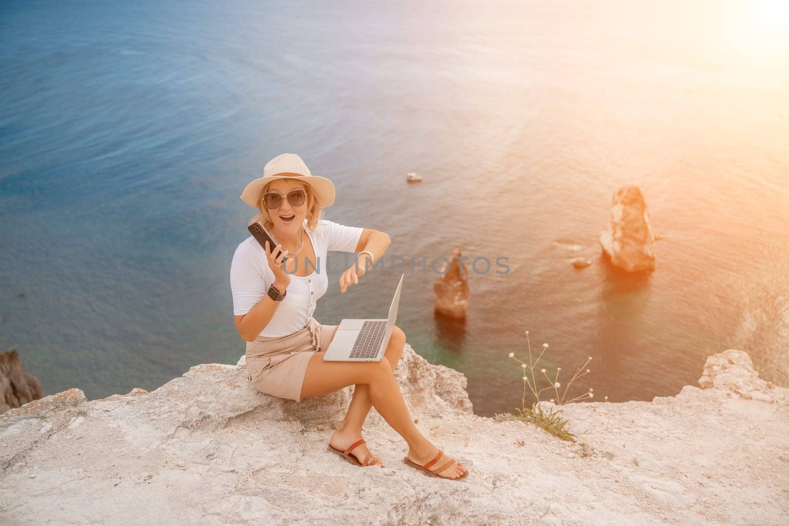 Freelance women sea working on the computer. Good looking middle aged woman typing on a laptop keyboard outdoors with a beautiful sea view. The concept of remote work. by Matiunina