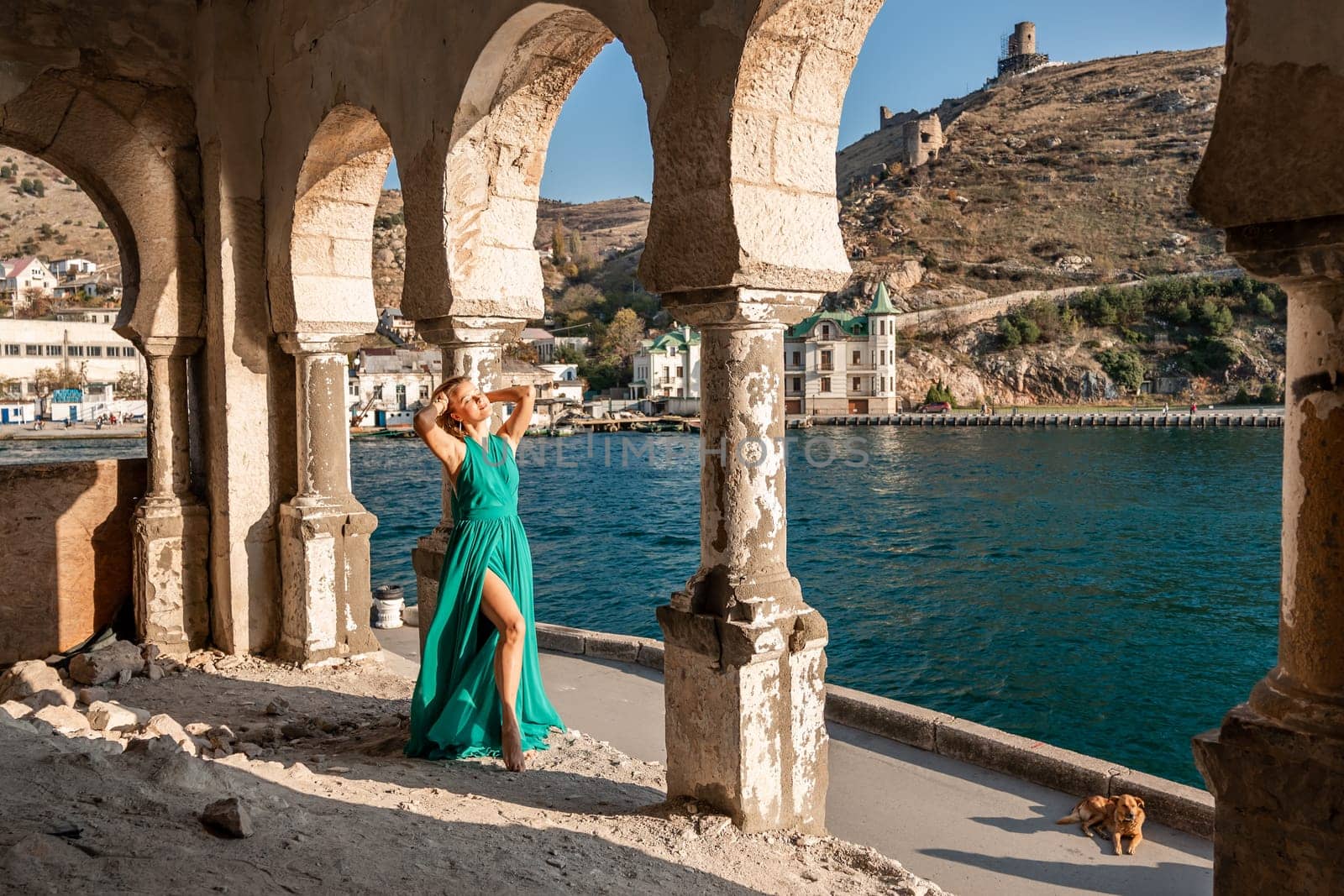 Woman dress sea columns. Rear view of a happy blonde woman in a long mint dress posing against the backdrop of the sea in an old building with columns. by Matiunina