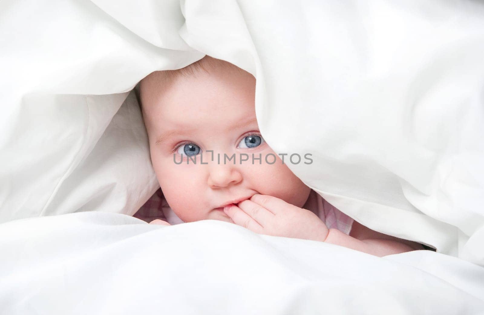 cute baby under a blanket in bed