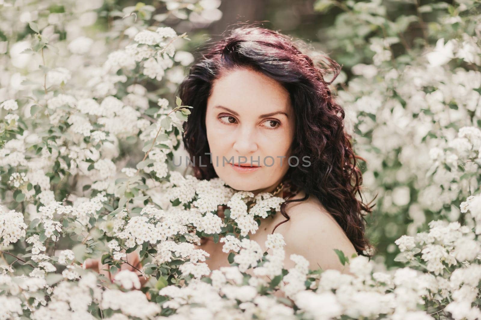 Woman spirea flowers. Portrait of a curly happy woman in a flowering bush with white spirea flowers. by Matiunina