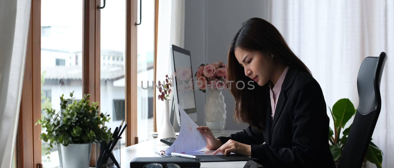 Serious female accountant comparing corporate income for previous year with current one at her workstation.