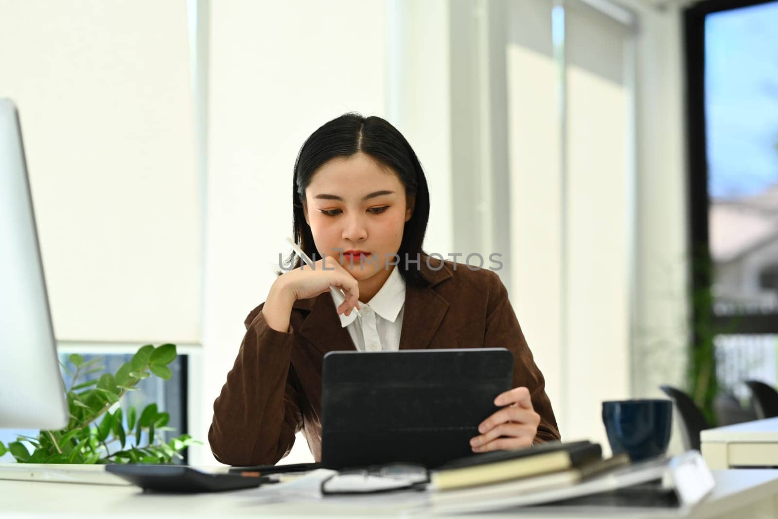 Focused asian woman entrepreneur using digital tablet working on investment and marketing projects at office.