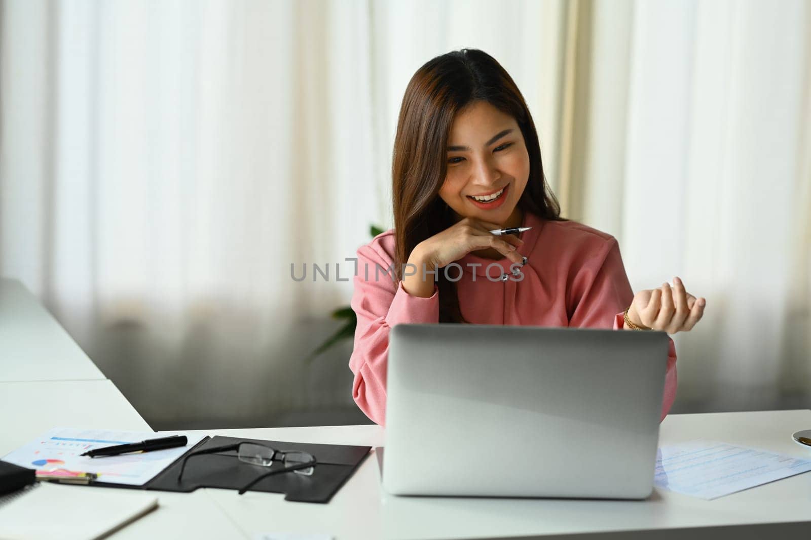 Friendly asian female entrepreneur talking on video call, consulting client distantly via laptop at workplace