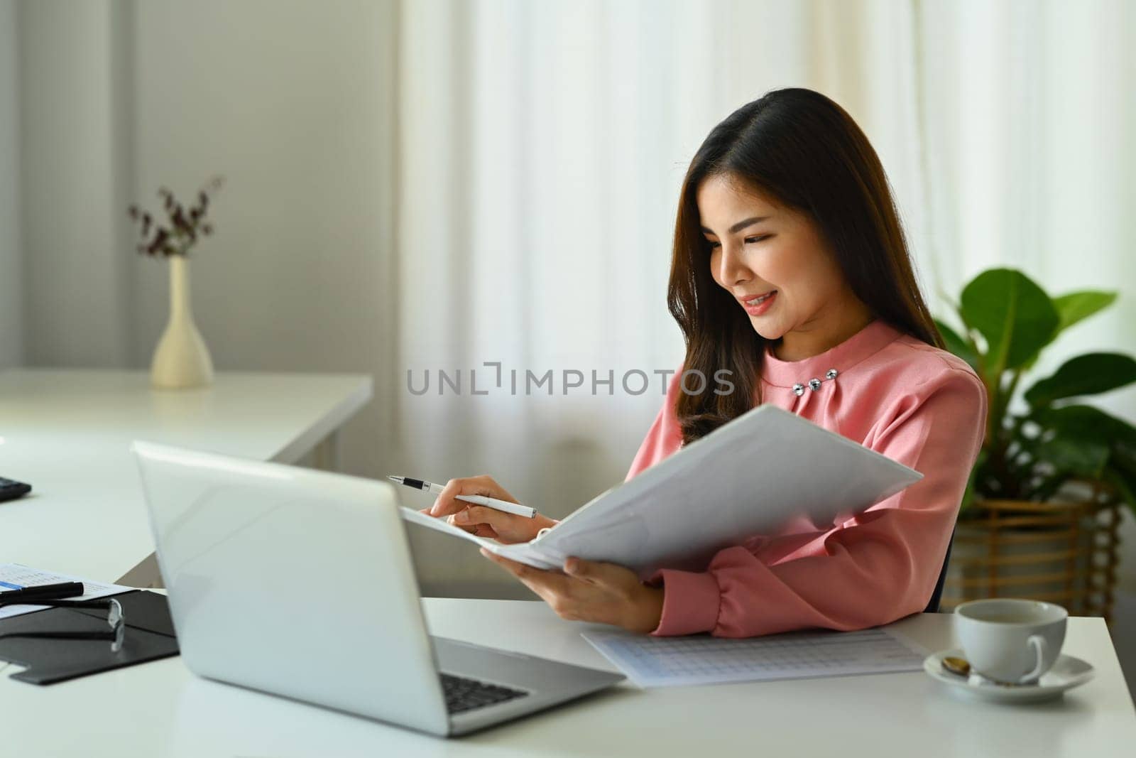 Asian businesswoman using laptop, working on investment and marketing projects at modern office.