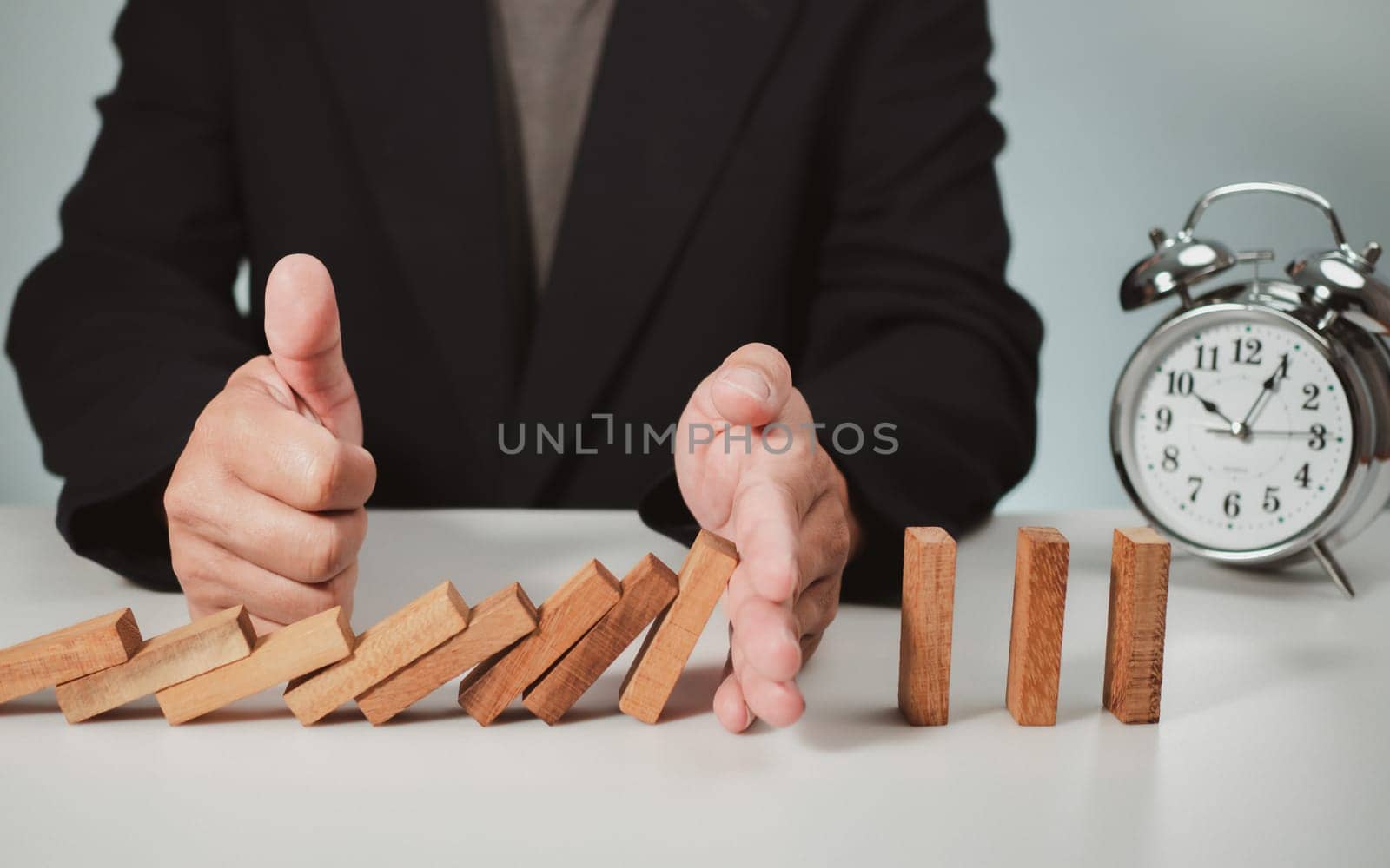 Risk management concept. Businessman hand stopping dominoes effect for business.  by Unimages2527