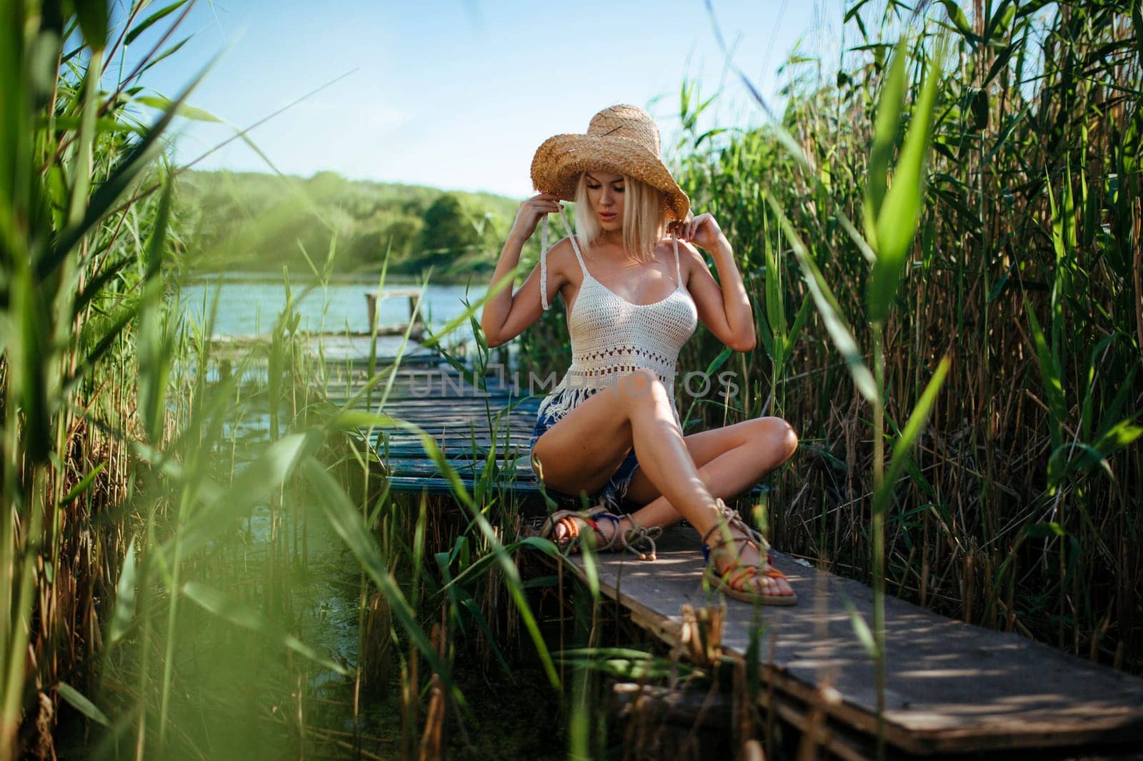 Beautiful model girl posing on the field enjoying nature outdoors in a straw hat. Beauty blond young woman with long straight blond hair .