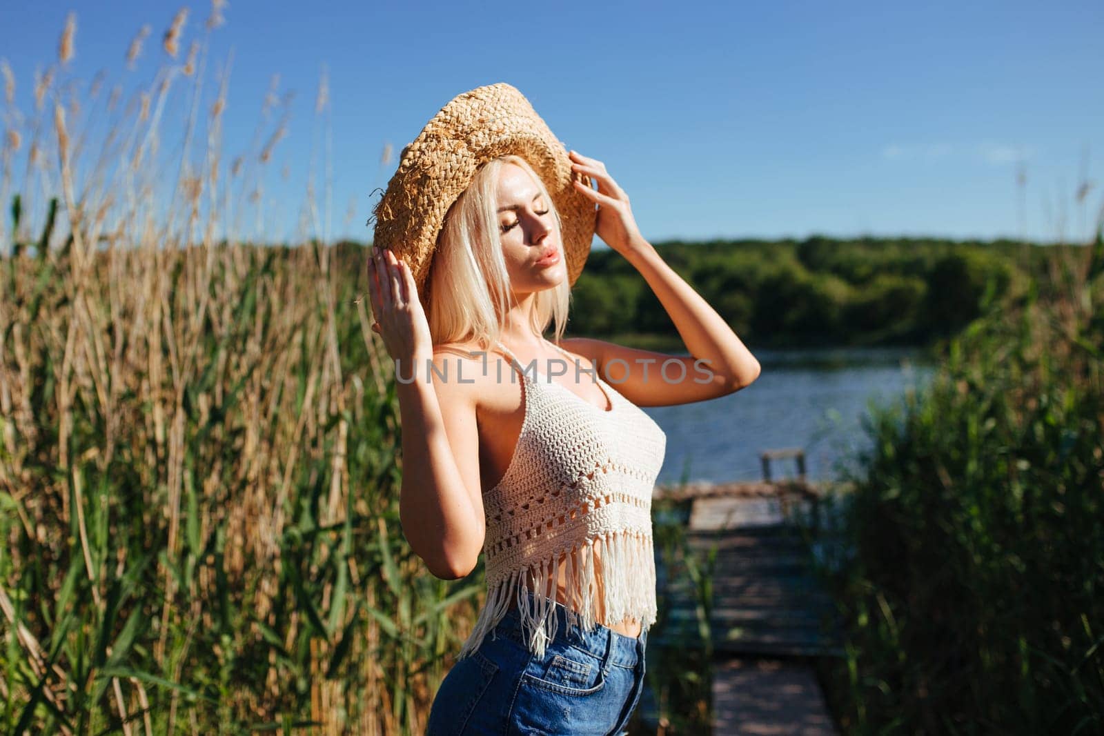 Beautiful model girl posing on the field enjoying nature outdoors in a straw hat. Beauty blond young woman with long straight blond hair close up portrait.