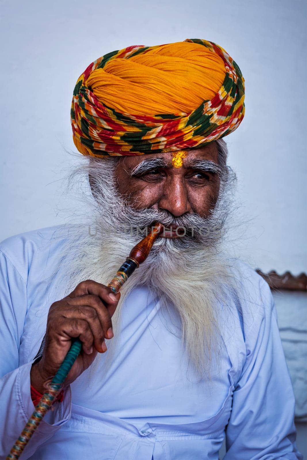 Old Indian man smokes hookah waterpipe in Mehrangarh fort by dimol