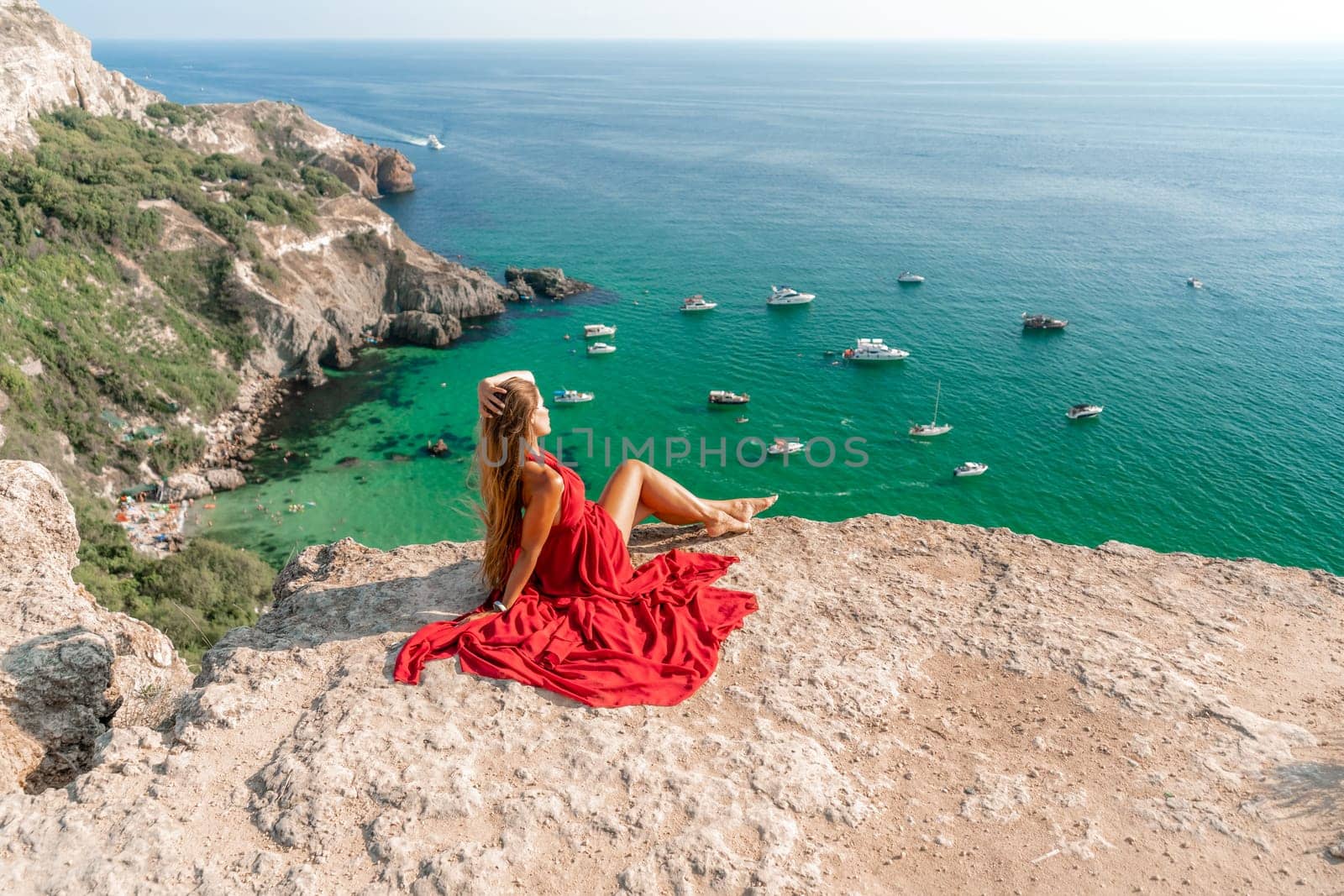 Woman sea red dress yachts. A beautiful woman in a red dress poses on a cliff overlooking the sea on a sunny day. Boats and yachts dot the background. by Matiunina