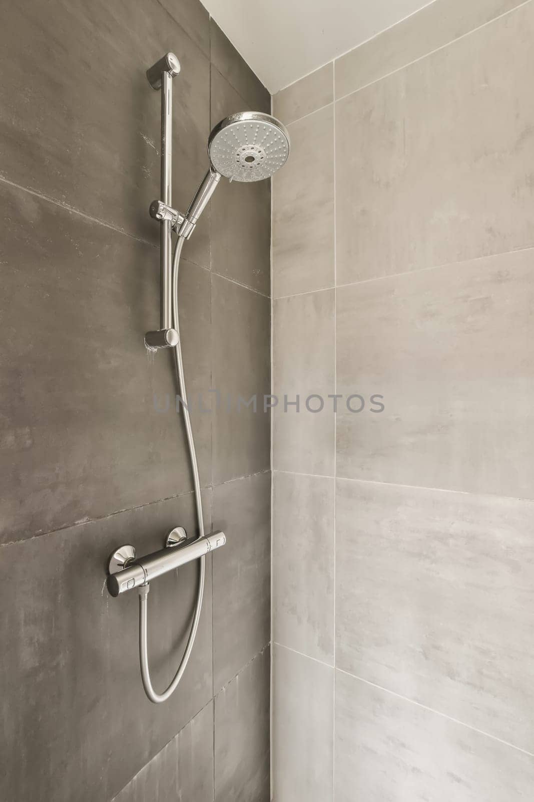 a shower with grey tiles on the wall and white tile flooring in a modern style bathroom interior stock photo
