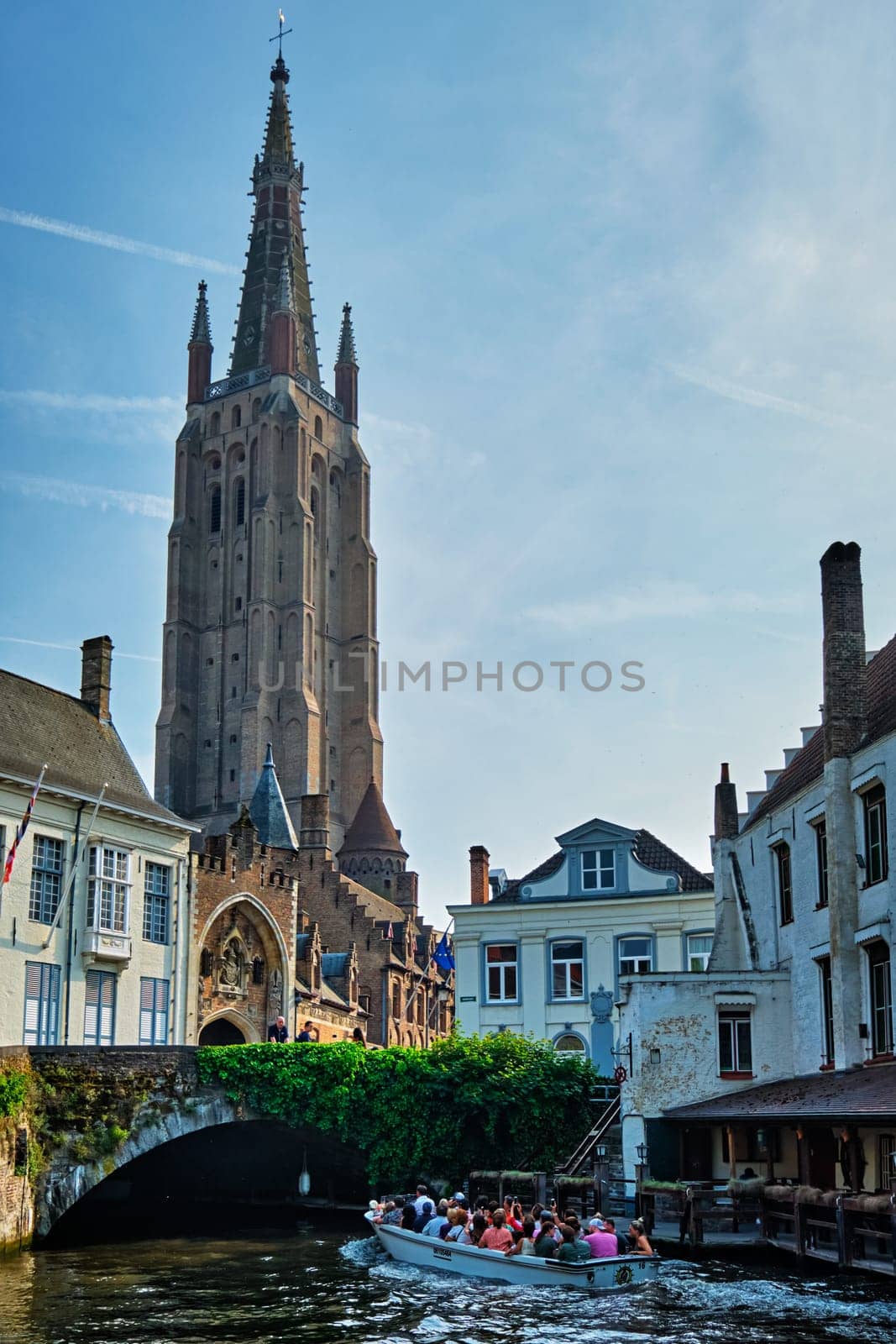 Bruges, Belgium - May 28, 2018: Tourist boat in canal near Church of Our Lady . Brugge Bruges, Belgium
