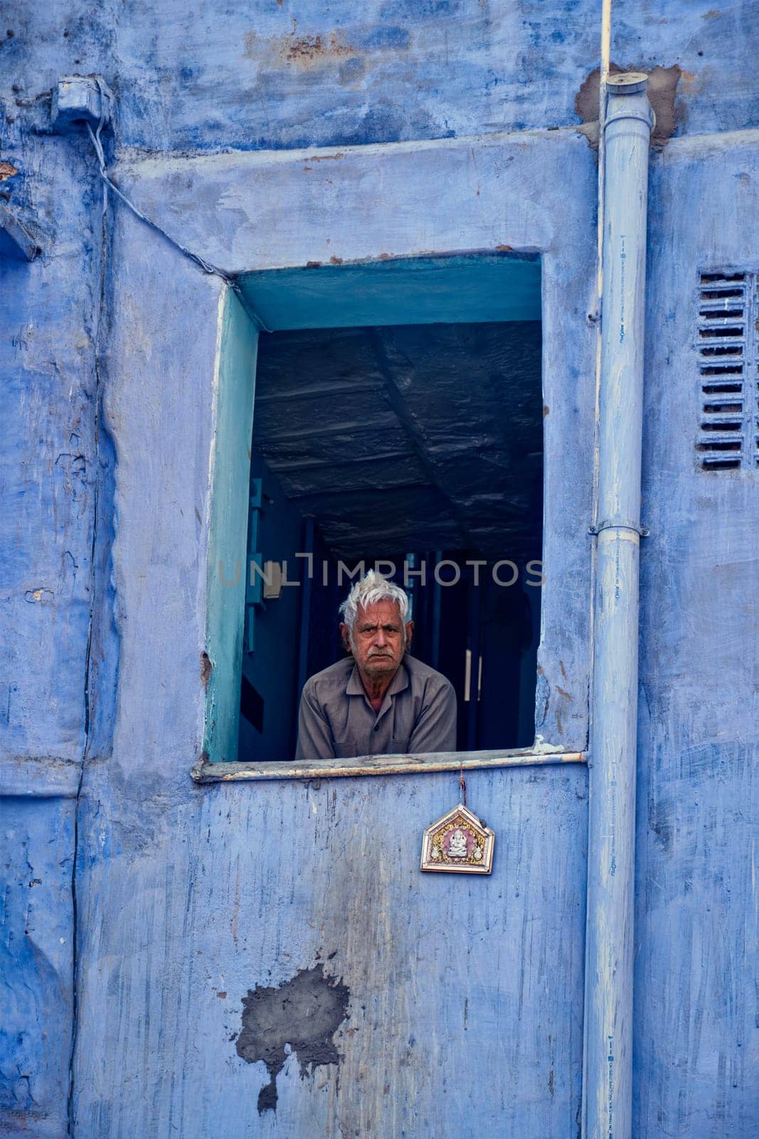 Jodhpur, India - November 13, 2019: Unidentified indian man in window of blue house in Jodhpur, also known as Blue City due to the vivid blue-painted Brahmin houses. Jodhpur, Rajasthan, India