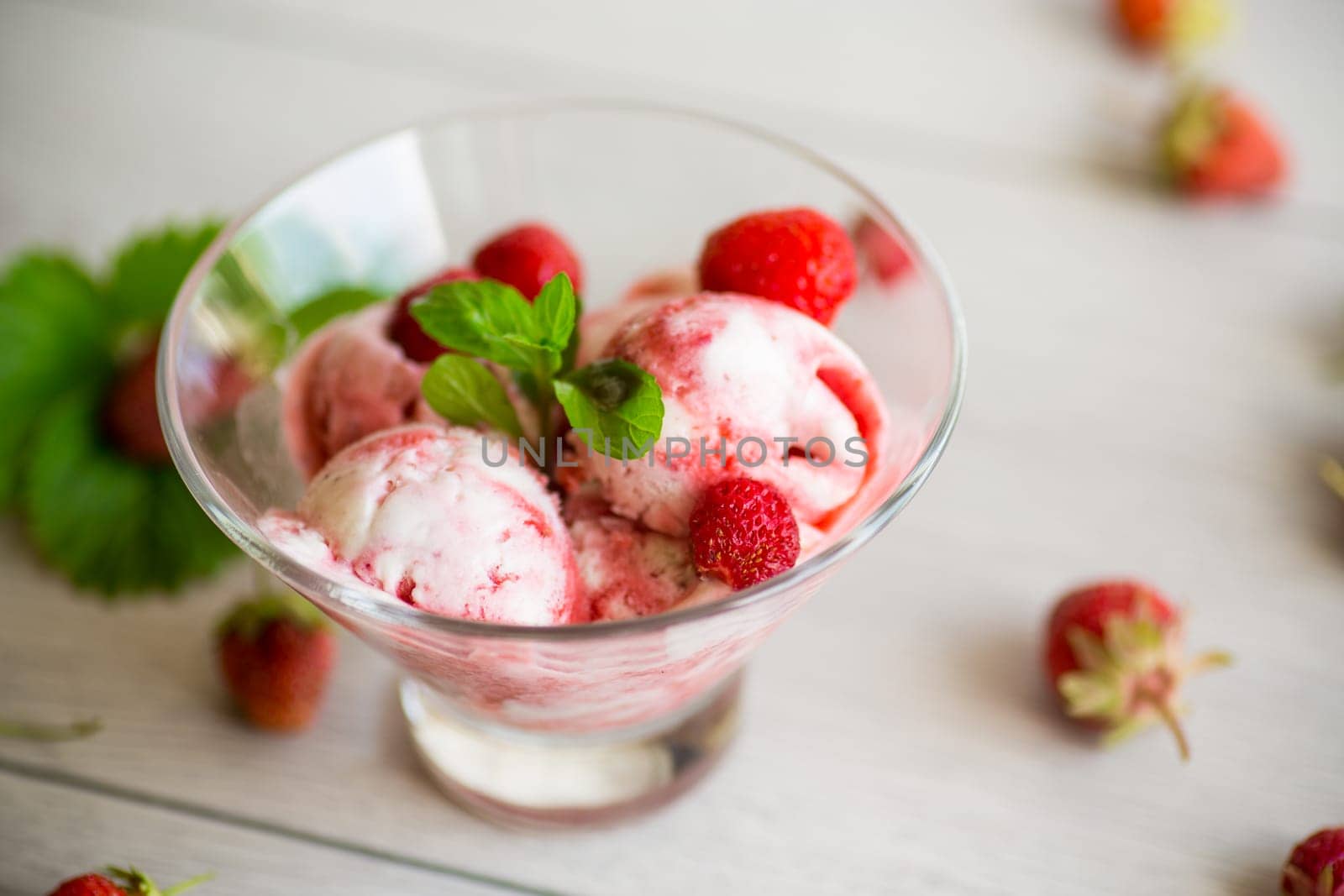 Balls of homemade strawberry ice cream in a bowl on a wooden table.