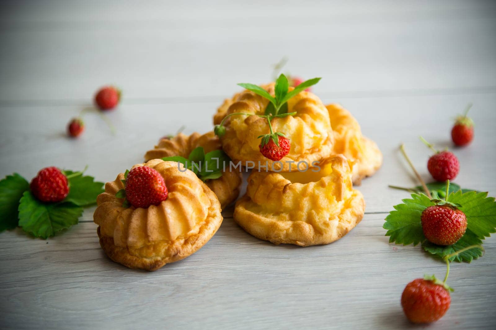 Cooked sweet curd cupcakes with fresh strawberries and mint on a wooden table.