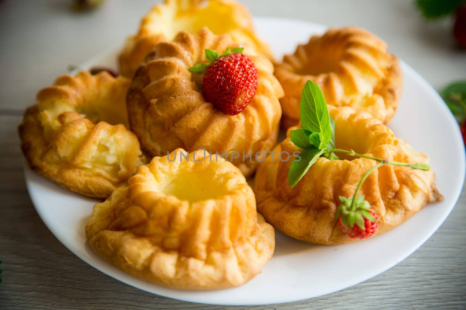 Cooked sweet curd cupcakes with fresh strawberries and mint on a wooden table.