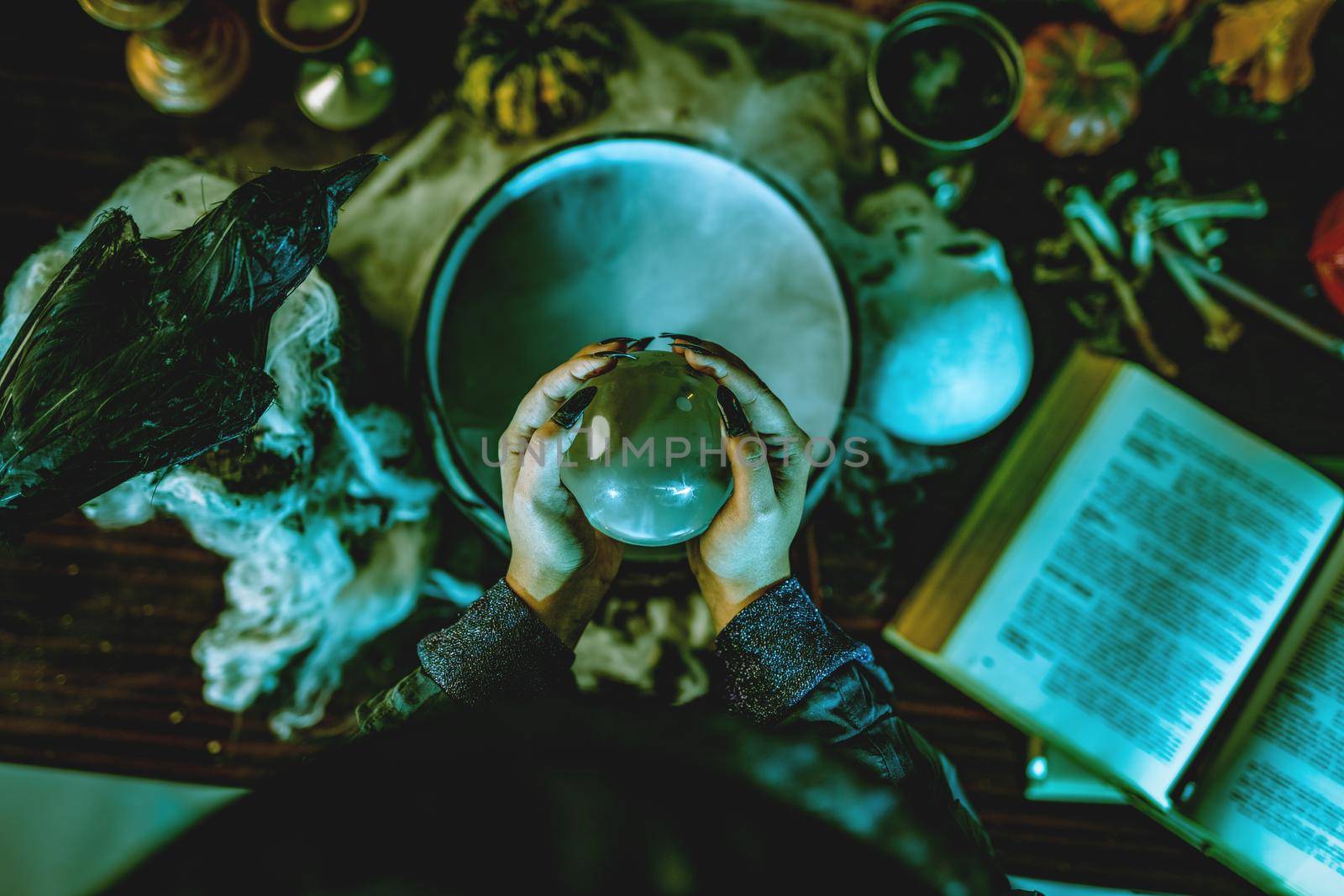 Top view of a magic ball in witch's hands above pot with poison potion.