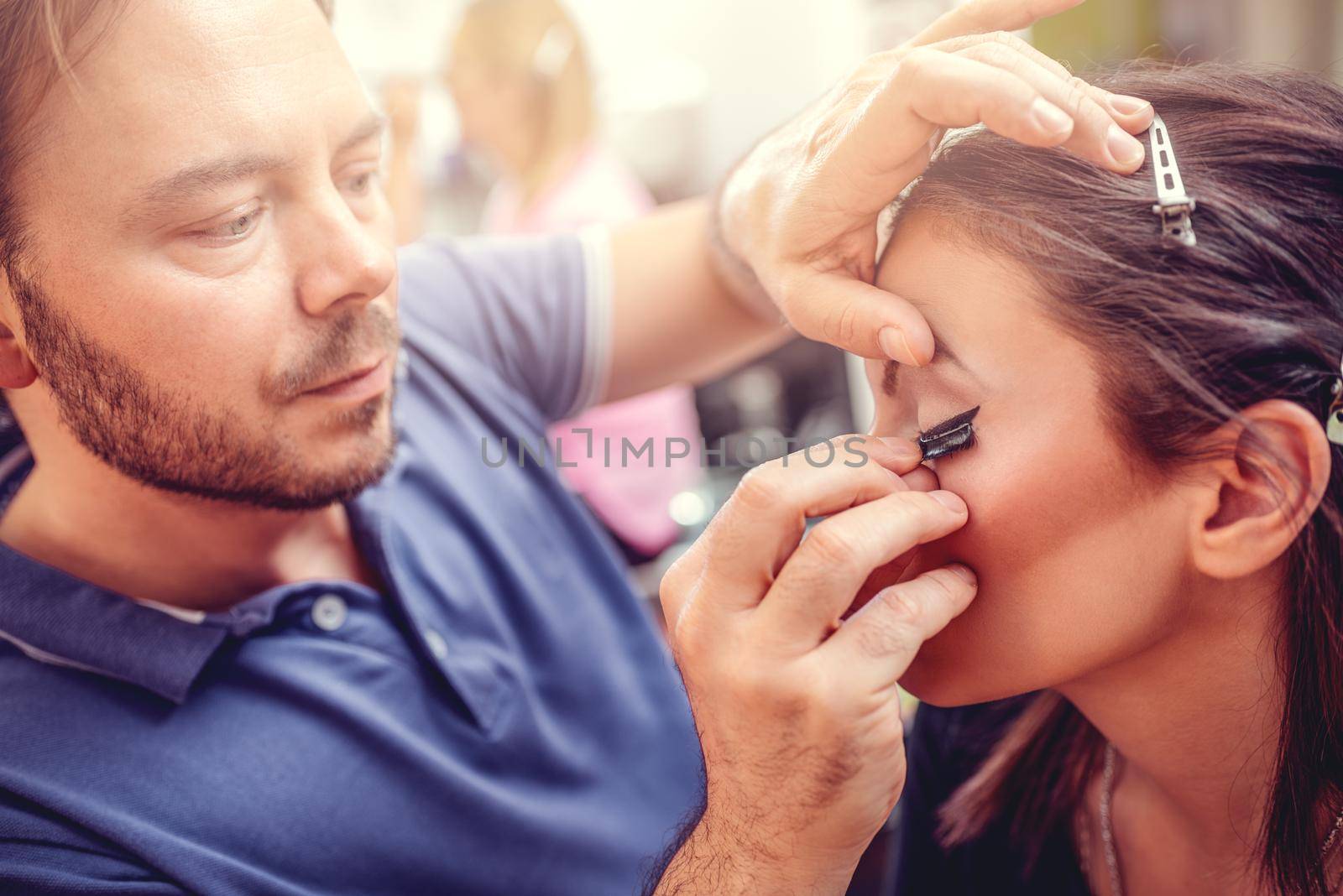 Make-up artist man applying the false eyelashes to model. Close up. 