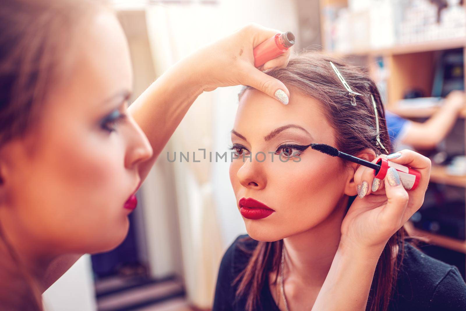 Make-up artist applying the mascara to a pretty model. Close-up. 