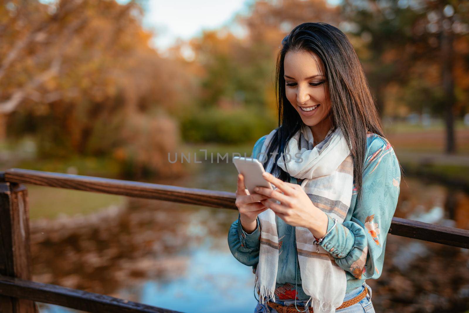 Happy young smiling woman reading message with pleasant news on smartphone in autumn nature.