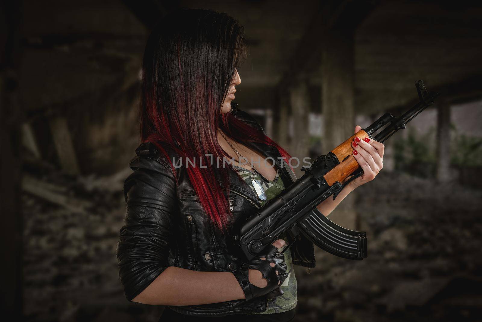 Profile of an attractive young woman in a leather jacket and camouflage shirt with cleavage with a kalashnikov in her hand.