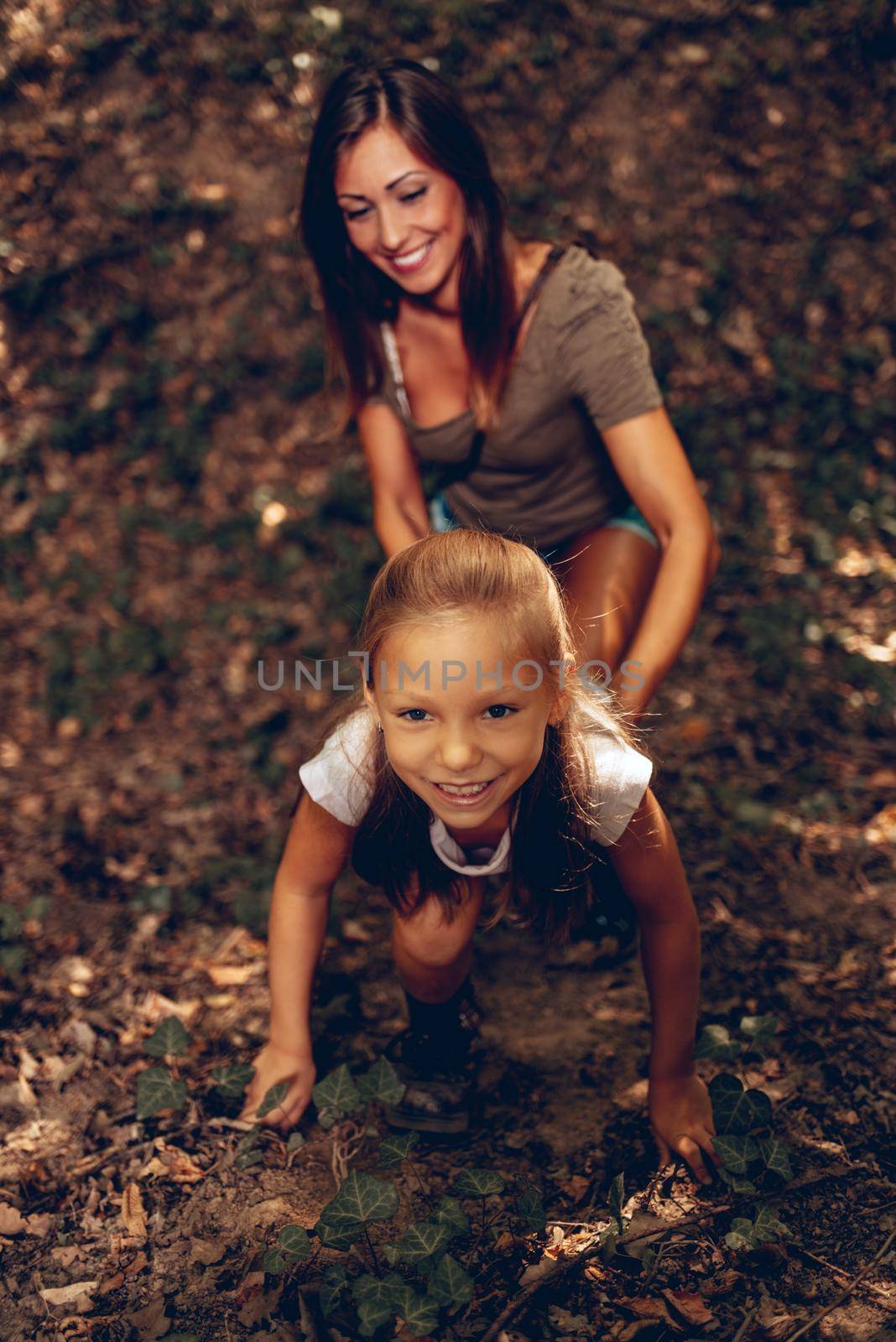 Beautiful young girl having fun in the forest. Mother looking on her.