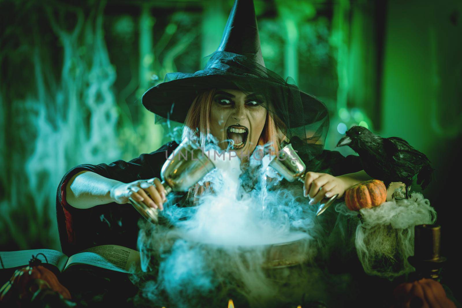 A witch in foggy surrounding holds two goblets above boiling water for a cooking poison soup.