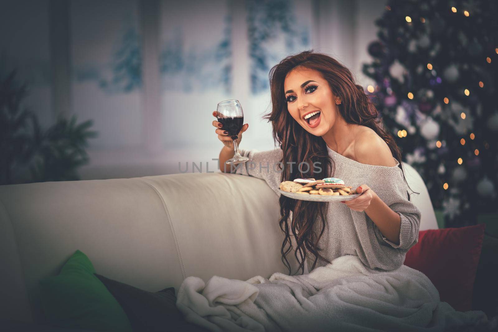 Beautiful smiling girl relaxing in bed with gingerbread cookie and glass of black vine.