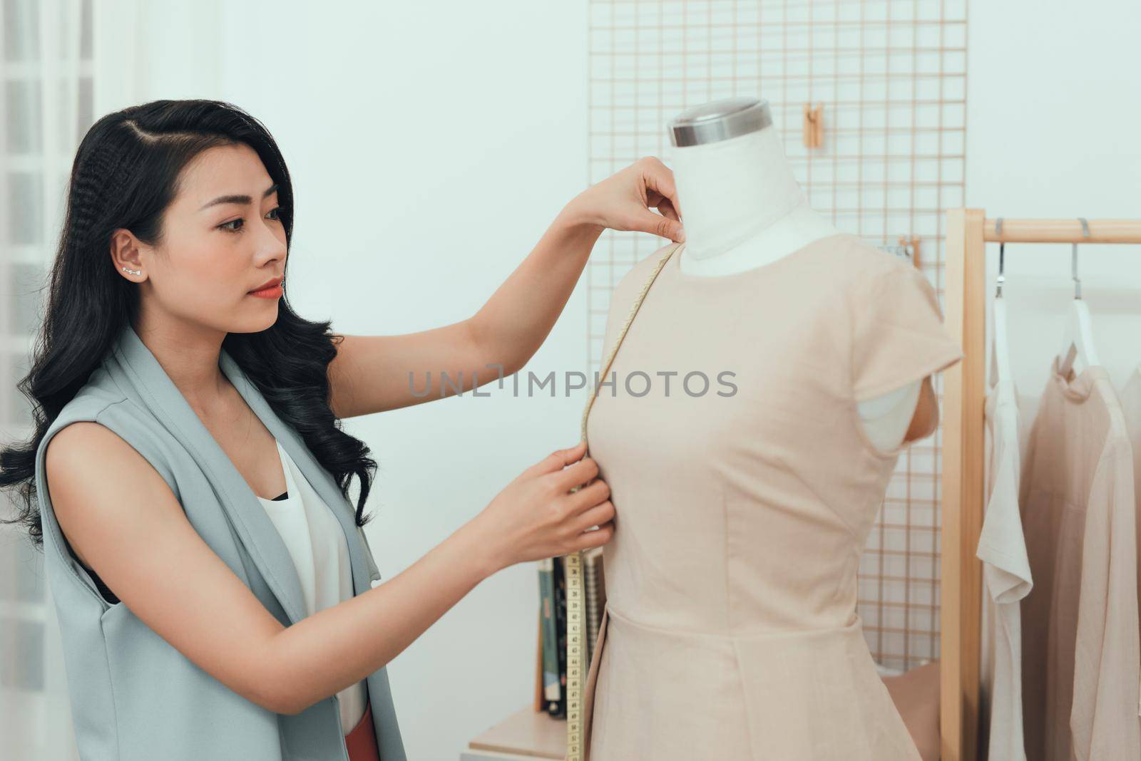 Young Asian female fashion designer taking measurements on mannequin in her studio