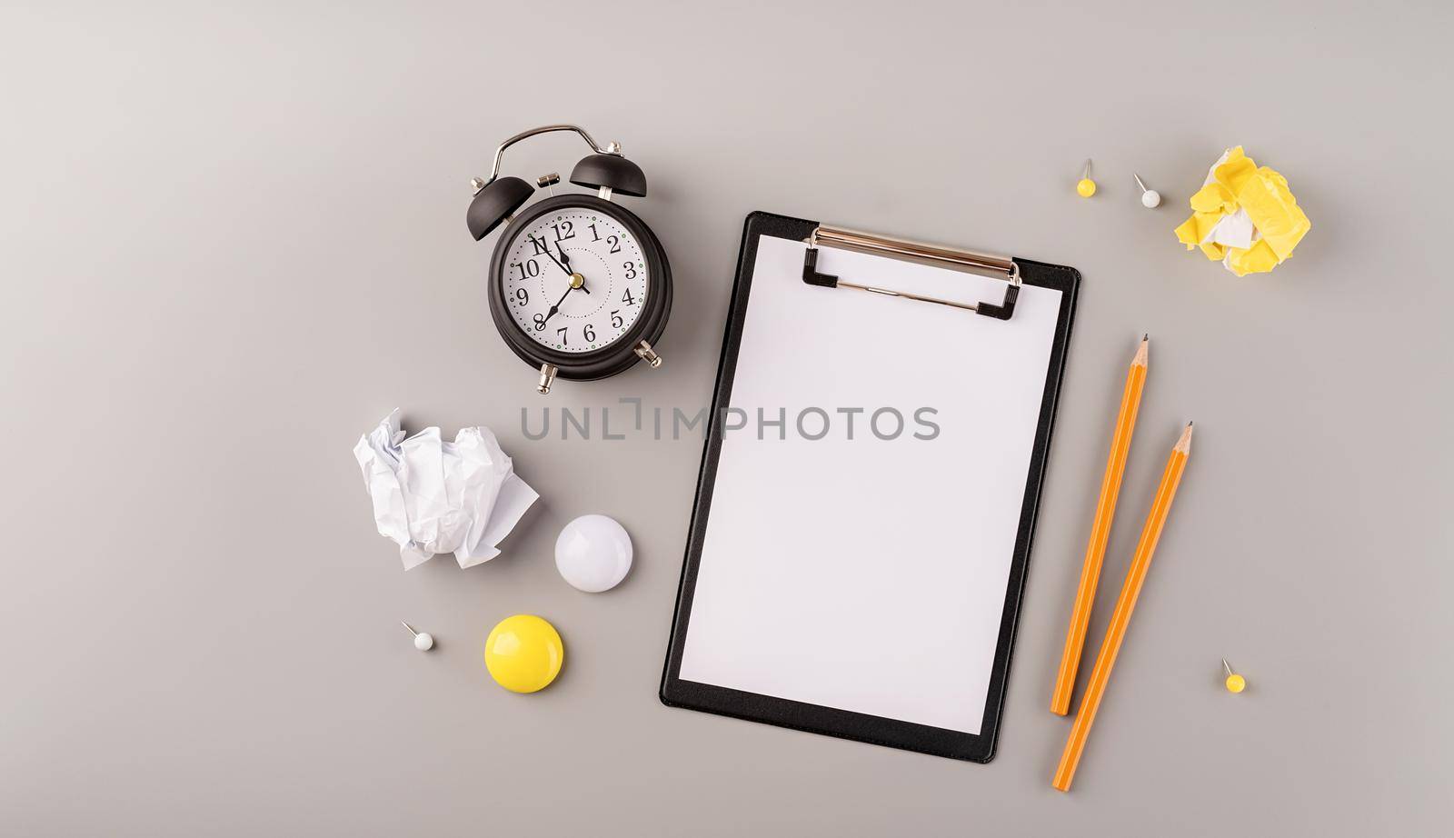 Business planning, time management concept. Blank paper on clipboard, white alarm clock and stationery top view on gray table. Copy space, flat lay