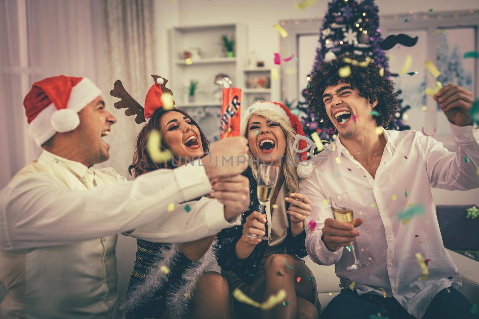 Two young cheerful couple celebrating Christmas with confetti at the home. They are having fun and toasting with champagne. 