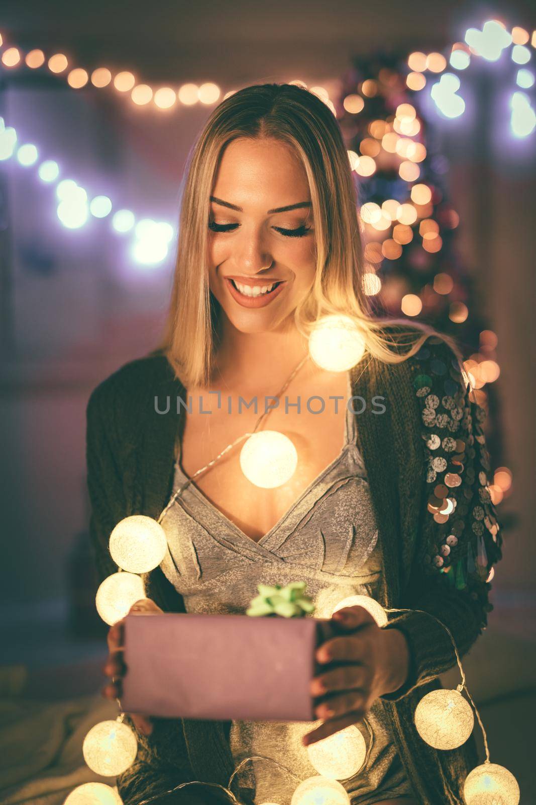 Cute young smiling woman holding gift surrounded with Christmas bubble lights. 