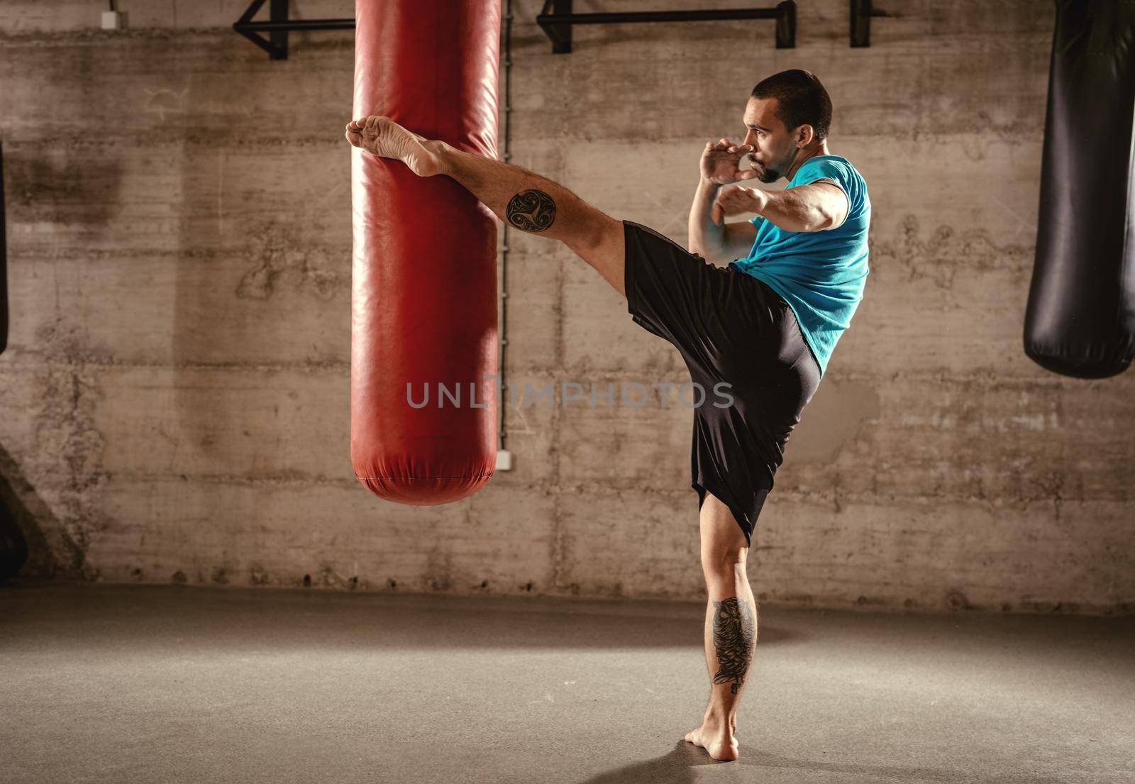 Muscular man punching with leg a boxing bag on cross fit training at the gym.