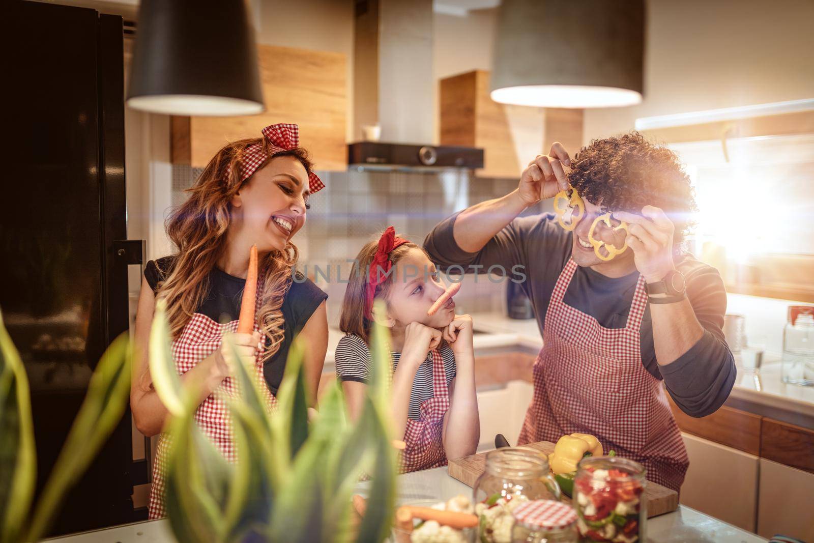 Happy parents and their daughter enjoy and having fun in making and having healthy meal together at their home kitchen.