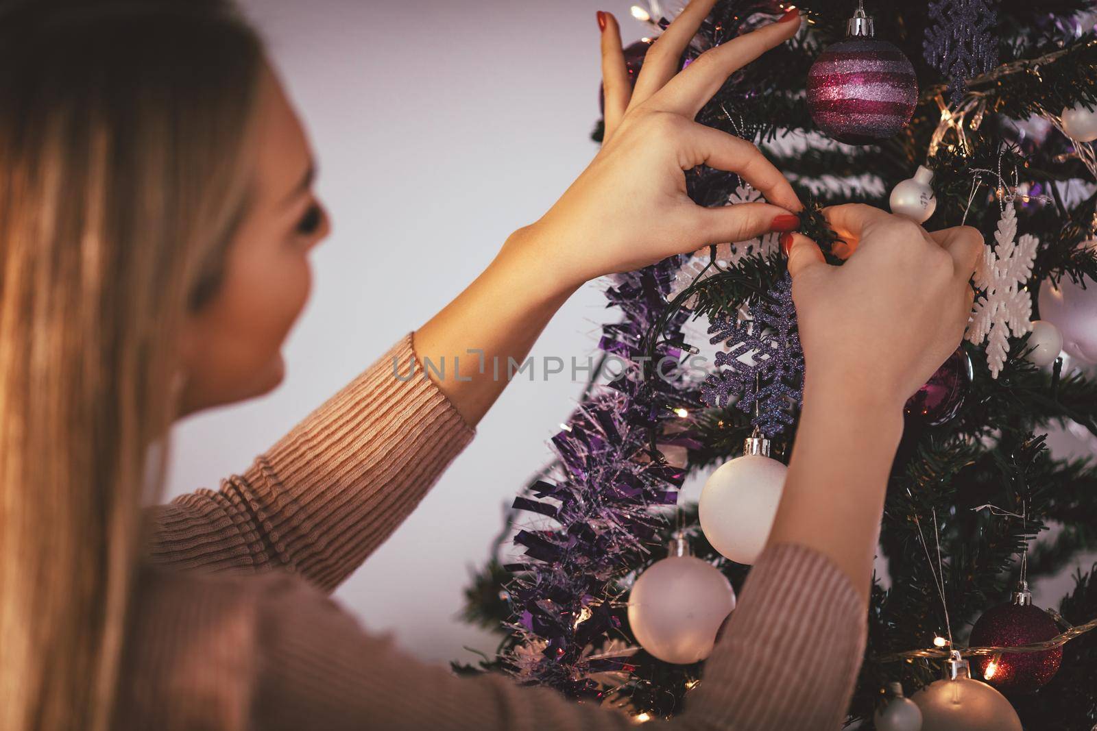 Beautiful smiling young woman decorating christmas tree with Christmas ornament at home.