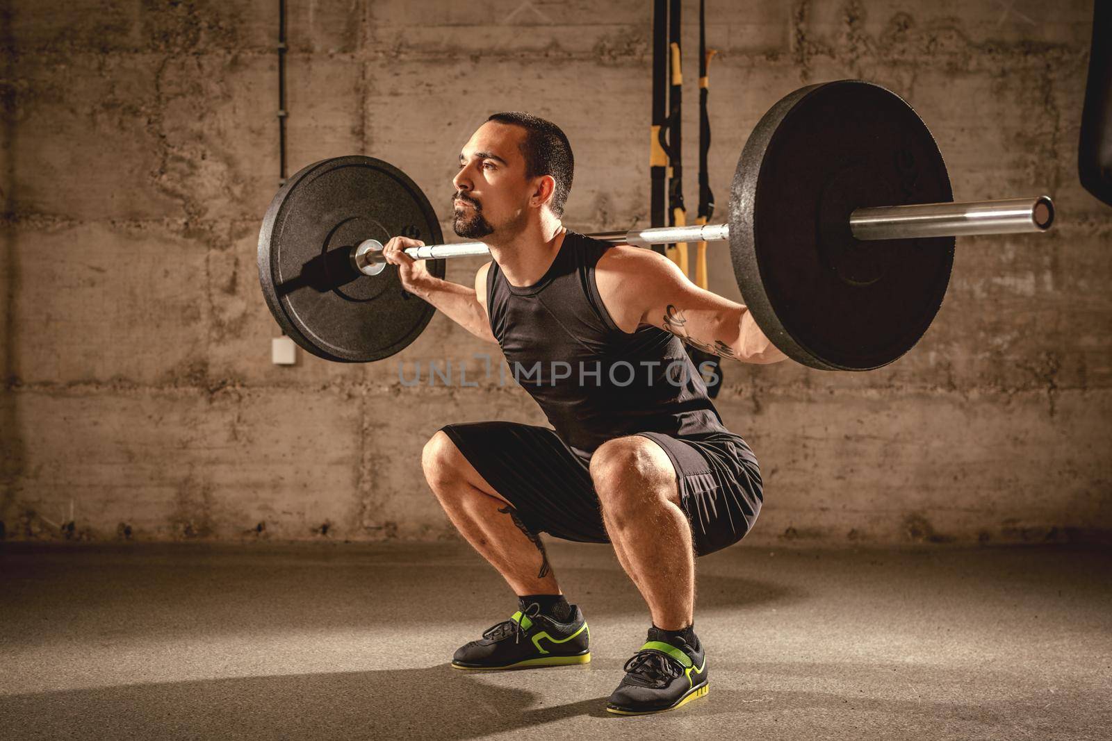 Handsome young muscular man doing squat exercise with barbell at the gym.
