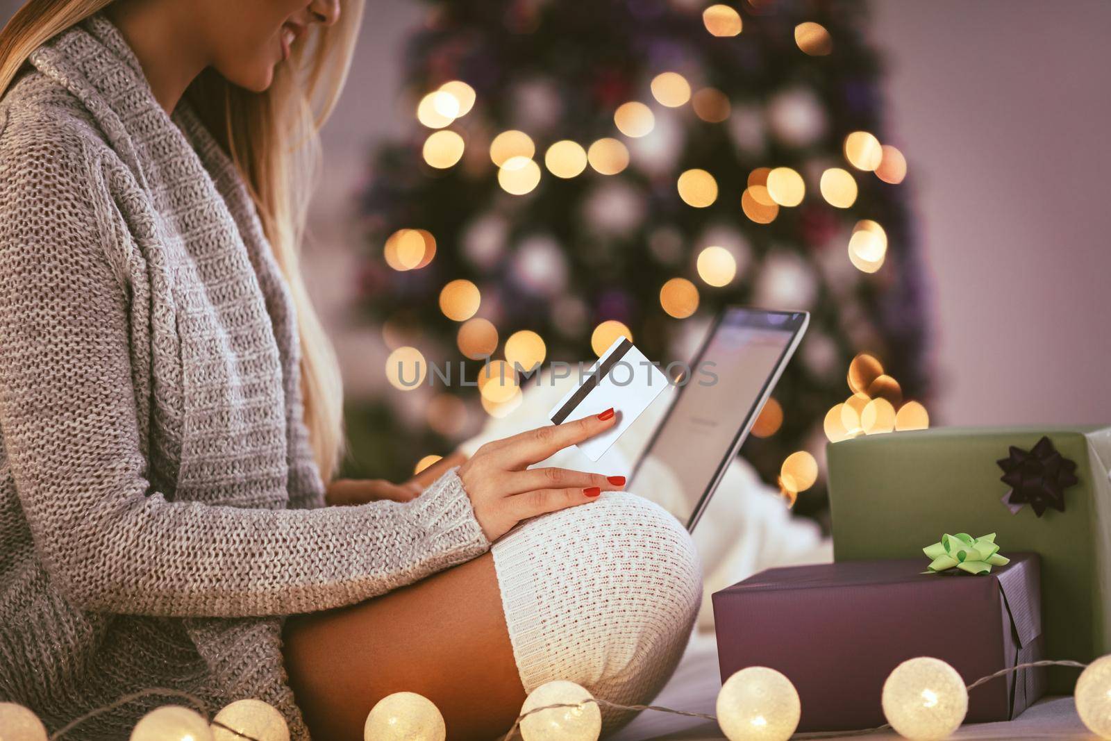 Happy young woman relaxing at home and online buying Christmas presents on laptop.