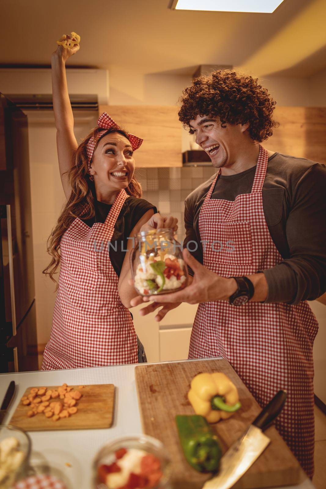 Cute couple is putting vegetables in a jar and smiling while making pickle in kitchen at home