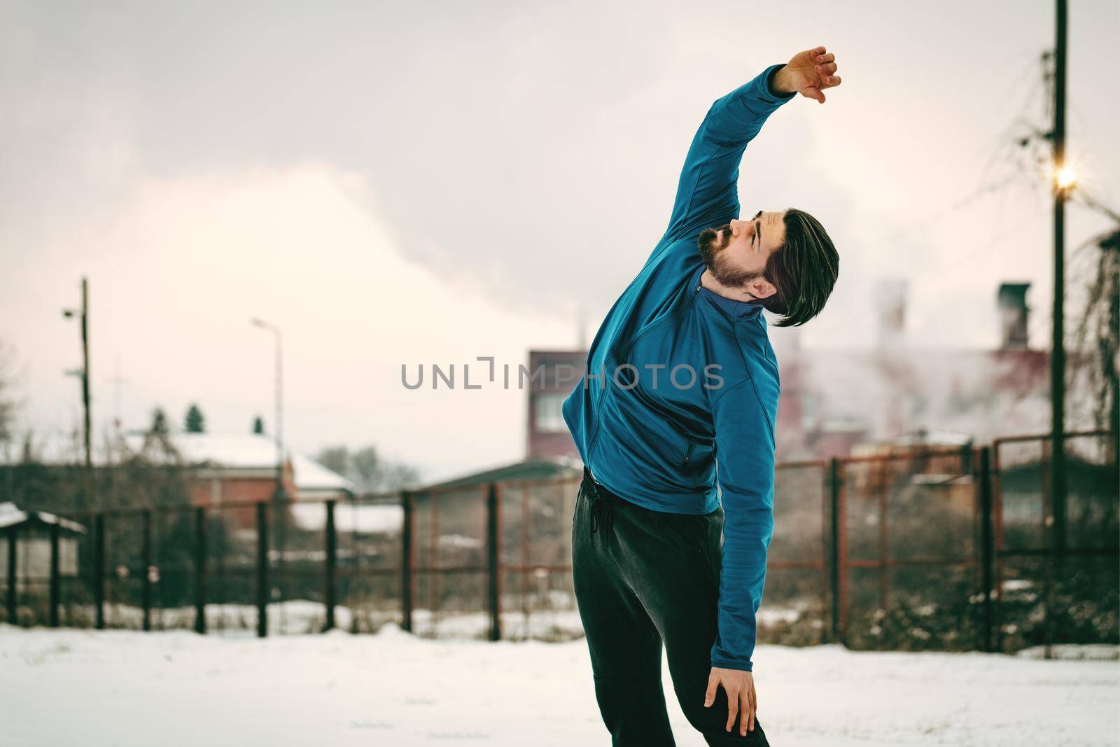 Active young man stretching and doing exercises in the public place during the winter training outside in. Copy space. 