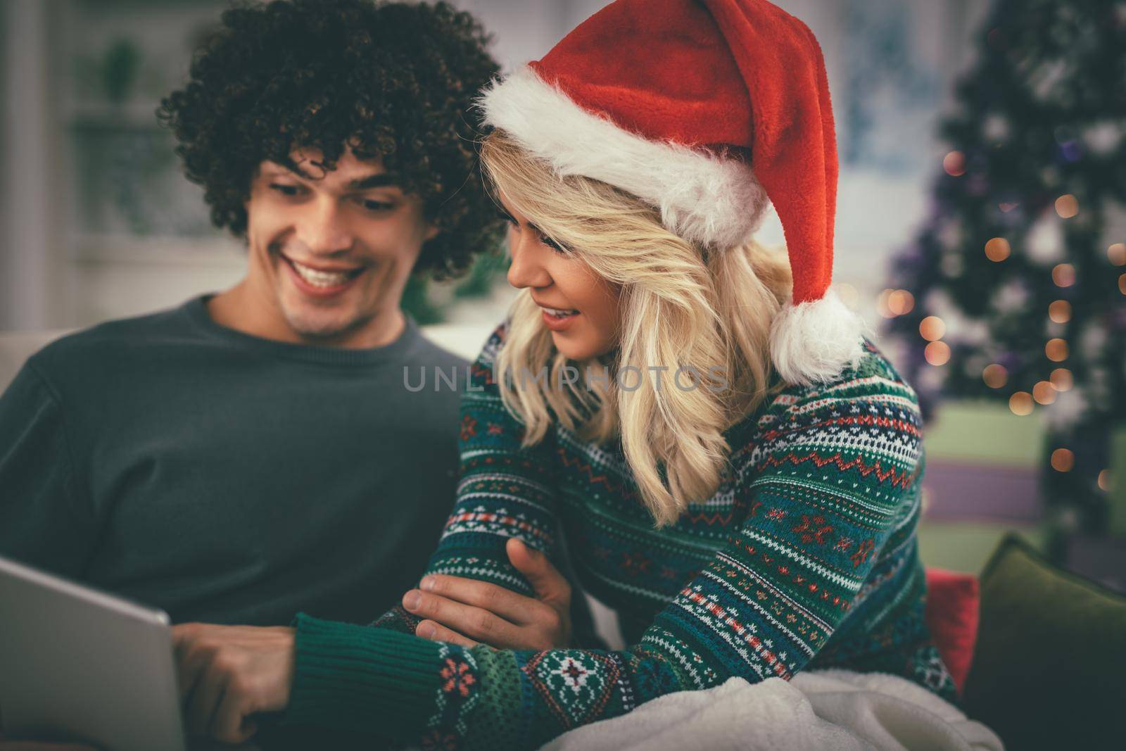 Cheerful young couple relaxing at home and online buying Christmas presents on laptop.