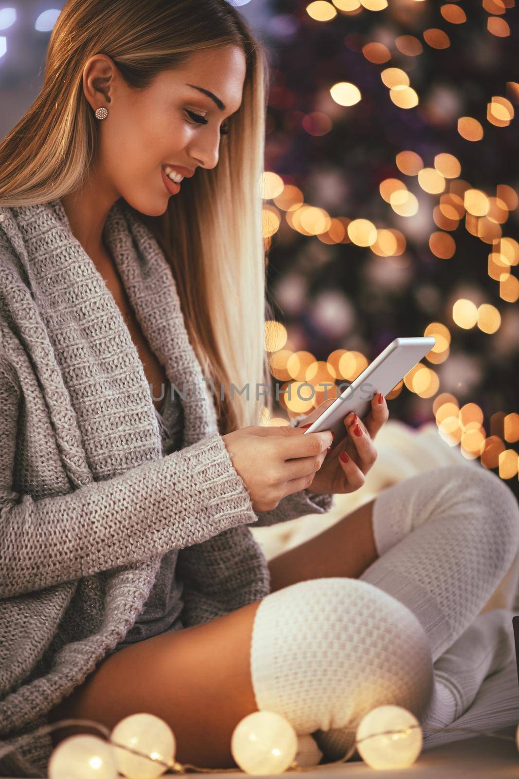 Cute young smiling woman using smarthphone and smiling during cozy Xmas holidays at home.