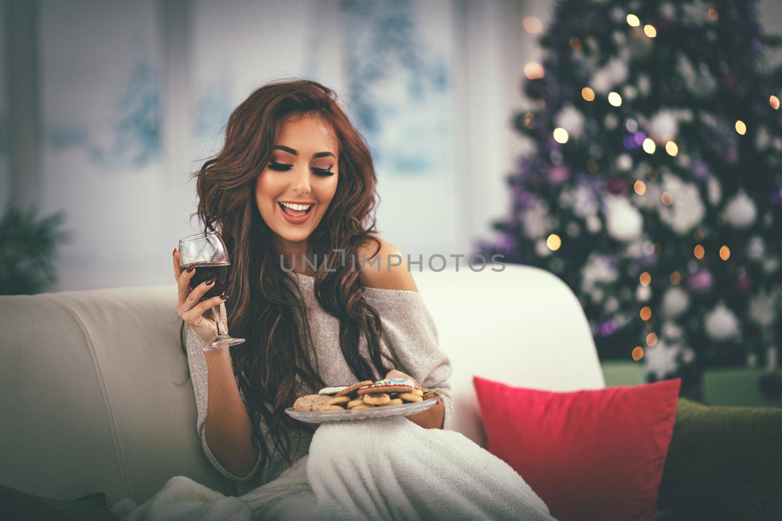 Beautiful smiling girl relaxing in bed with gingerbread cookie and glass of black vine.