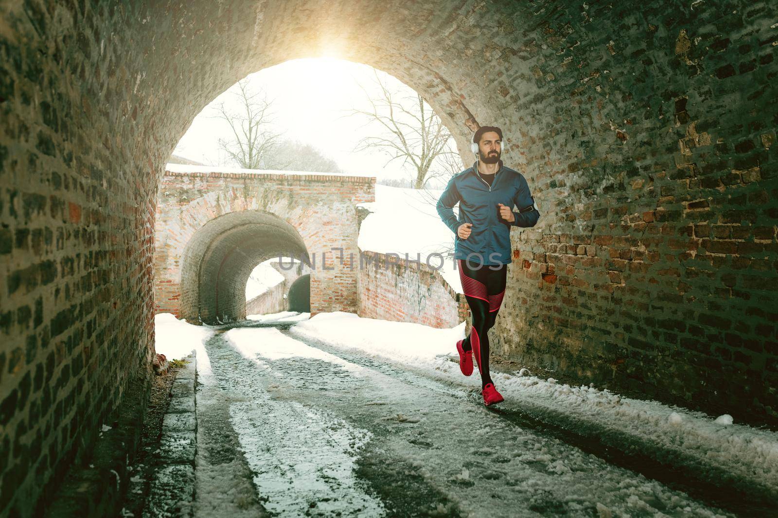 A male runner with headphones on his ears running in the public place during the winter training outside in. Copy space.